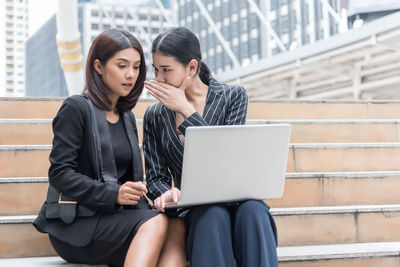 Female colleagues discussing over laptop while sitting on steps