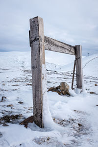 Wooden structure on snow covered field against cloudy sky