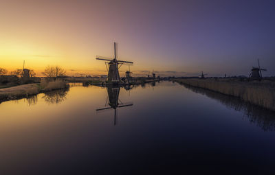 Lake by traditional windmills against clear sky during sunset