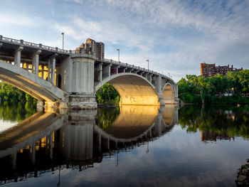 Arch bridge over river by buildings against sky