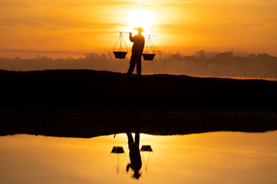 Silhouette man standing on lake against orange sky