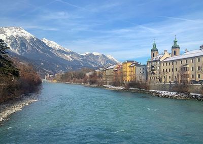 River amidst buildings against sky, with the alps mountain range as a backdrop