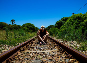 Woman sitting  on railroad track against clear blue sky