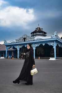Full length portrait of woman standing against historical building