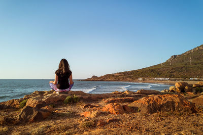 Woman sitting on rock at beach against clear sky