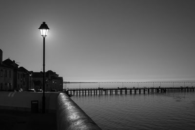 Illuminated street light by sea against sky