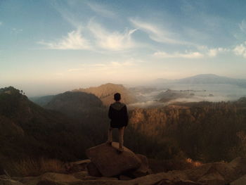 Rear view of teenage boy standing on mountain against sky