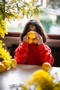 Portrait of sitting at the table girl hiding herself behind lemons