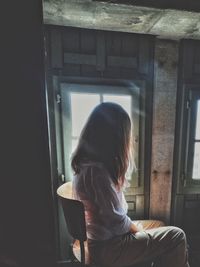 Side view of woman looking through window at home