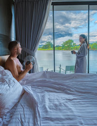 Rear view of woman sitting on bed at home