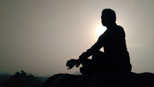 Silhouette man sitting against sky
