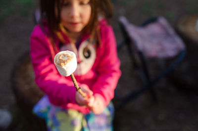 High angle view of girl holding marshmallow on stick while sitting at campsite