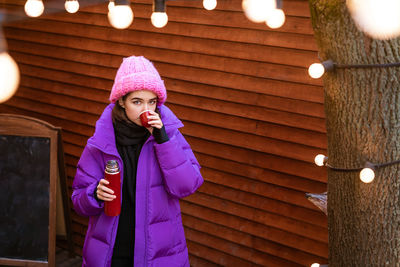 A positive woman spends time outdoors in frosty weather, drinks a hot drink