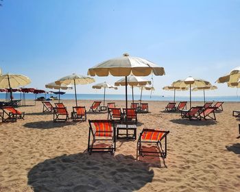 Deck chairs on beach against sky