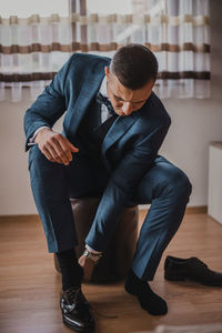 Full length of man sitting on hardwood floor at home