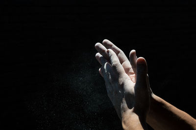 Close-up of cropped hands cleaning dust against black background