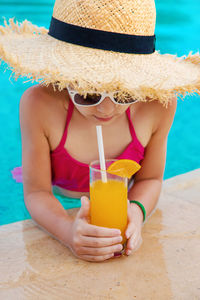 Girl wearing sunglasses drinking orange juice at poolside