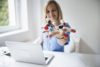 Smiling doctor holding molecular structure at clinic