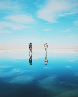 Reflection of friends on sea against sky