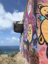 Graffiti on stone wall by sea against sky