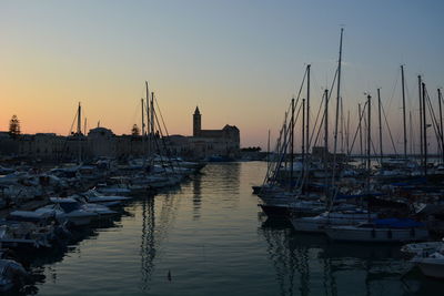 Sailboats moored at harbor against sky during sunset