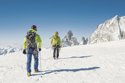 Rear view of hikers with rope walking on snow covered mountain against clear blue sky