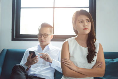 Man using mobile phone while sitting by angry woman on sofa at home