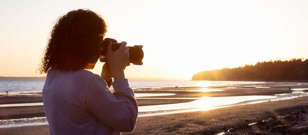 Woman looking at sea against sky during sunset