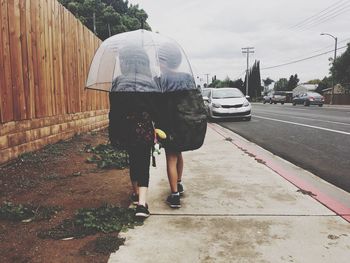 Rear view of backpack siblings walking under umbrella on footpath
