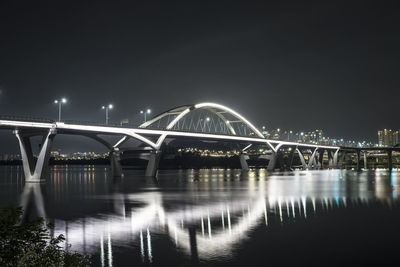 Illuminated bridge over river against sky at night