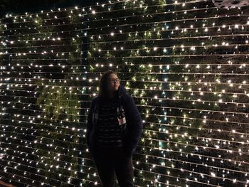 Full length portrait of young woman standing against illuminated building