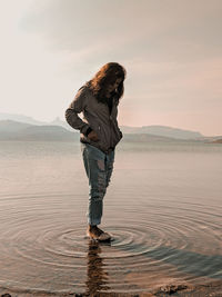 Woman standing in sea against sky during sunset