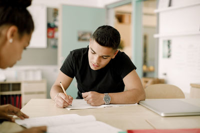 Male teenager writing while sitting in classroom