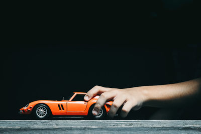 Cropped image of hand holding toy car against black background