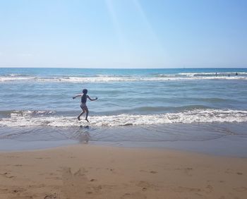 Boy jumping over sea against blue sky
