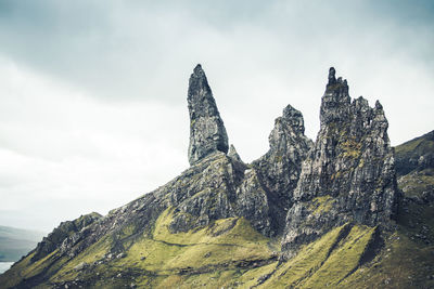 Low angle view of rocks on mountain against cloudy sky