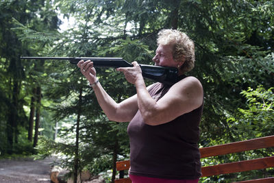 Side view of senior woman holding umbrella against trees in forest