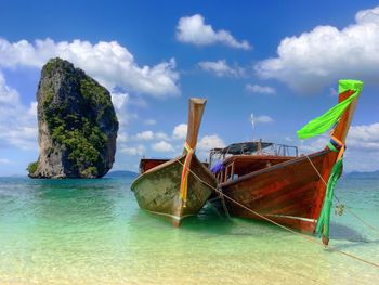 Boats moored on exotic beach against sky and limestone