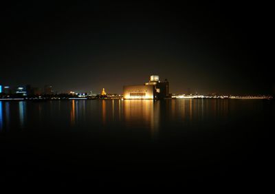 Illuminated buildings by sea against clear sky at night