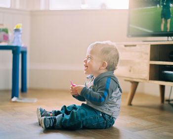 Side view of cute boy sitting on floor at home