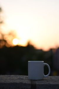 Close-up of coffee cup on table against sky during sunset