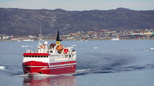 People sailing on sea by mountains against sky