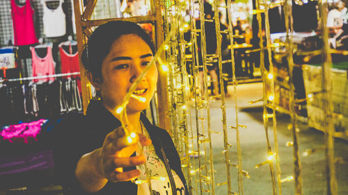 Smiling young woman holding illuminated string light 