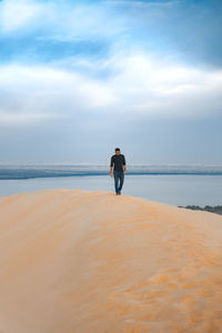 Rear view of woman standing at beach against sky