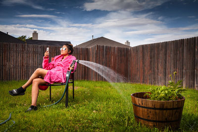 Woman sitting on seat in yard against sky