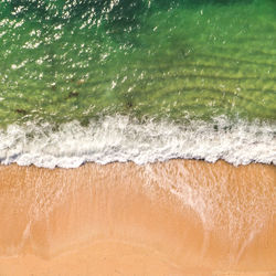 Aerial view of white waves rolling over sandy beach and emerald green ocea