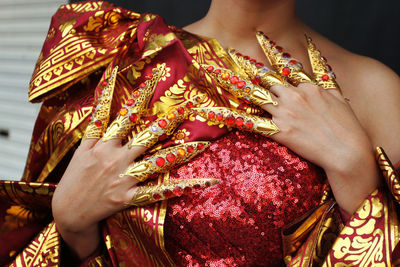 Pose of a lady showing off her long golden nails over her shiny red beaded dress.