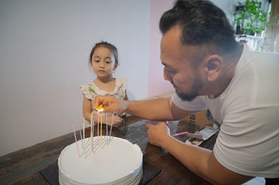 Lighting candles on birthday cake with little girl watching.