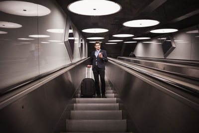 Low angle view of businessman with luggage on escalator in airport