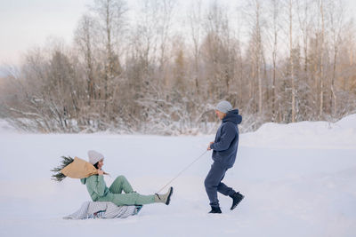 Smiling man giving sledding ride to woman. love and leisure concept.